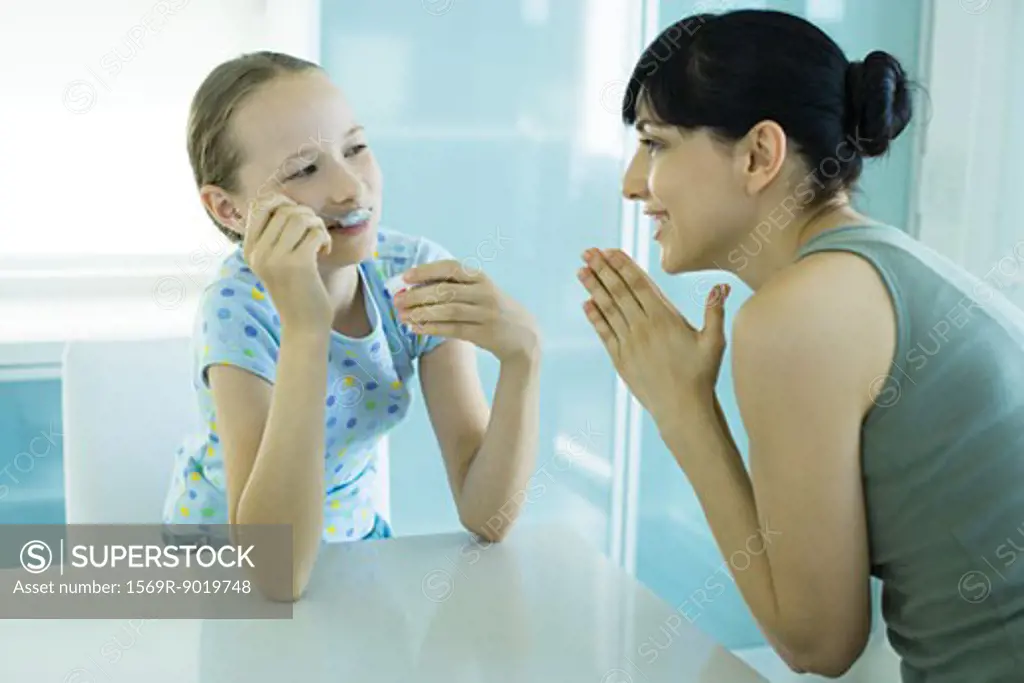 Girl eating ice cream dessert, woman looking at girl with hands clasped