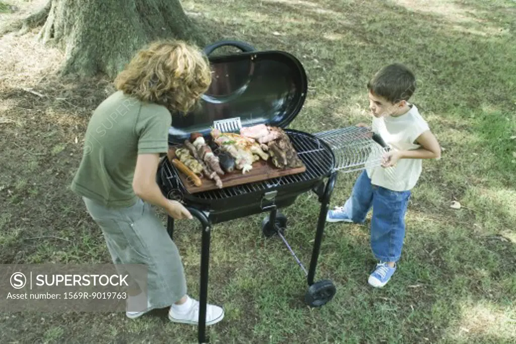 Two boys standing next to tray of grilled meat on barbecue