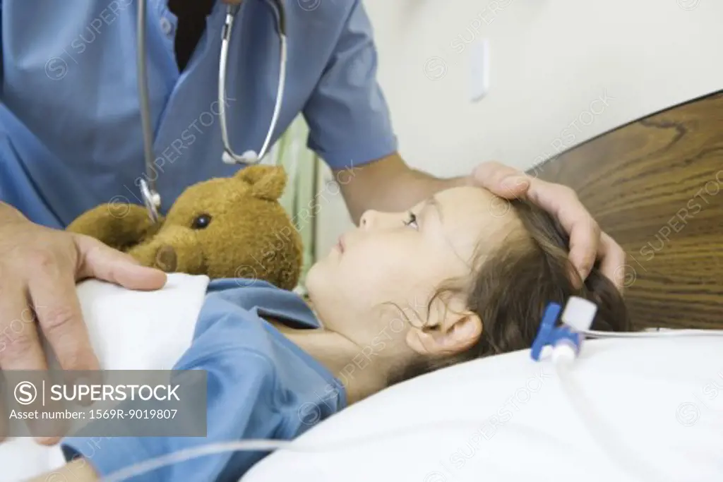 Girl lying in hospital bed, male nurse's hand on girl's head