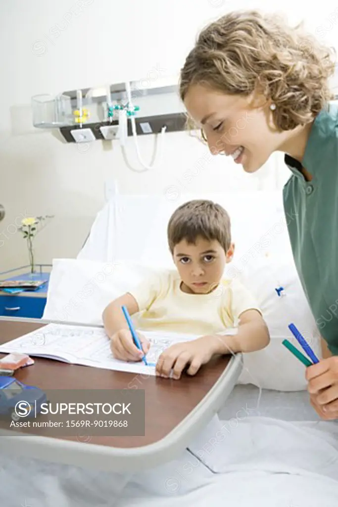 Boy lying in hospital bed, coloring