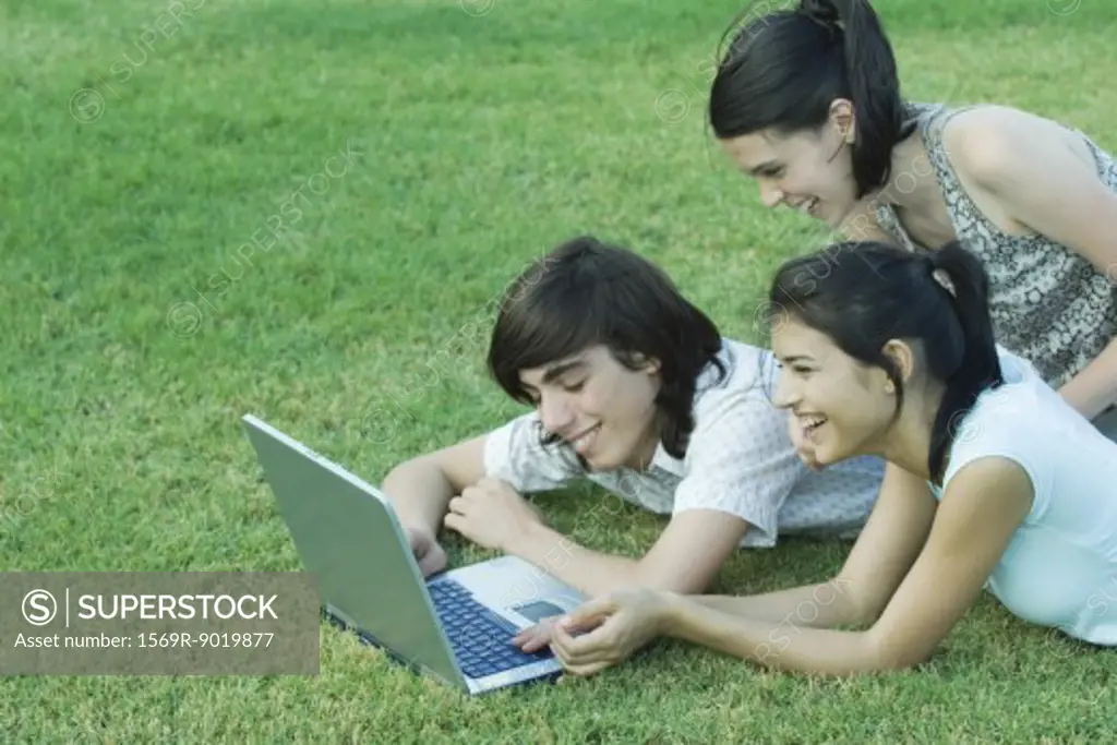 Young friends lying in grass, using laptop together