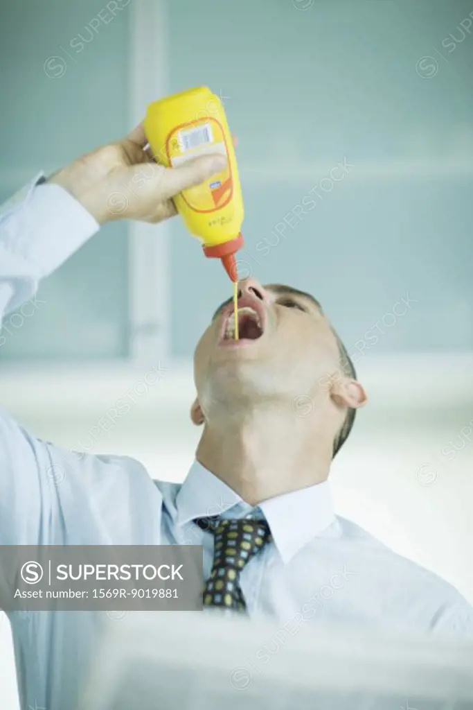 Man squeezing mustard into mouth
