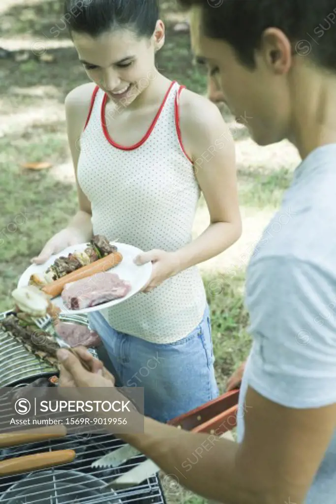Man serving teen girl grilled meats from barbecue