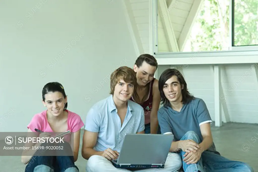 Four teen friends sitting on floor together, using laptop