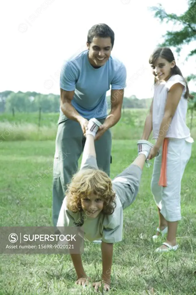 Family outdoors, father and sister holding boy's legs like wheelbarrow