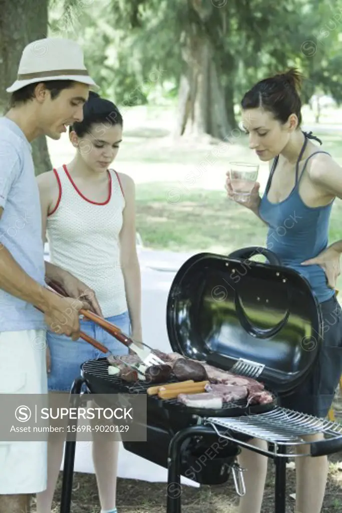 Man grilling meats on barbecue while woman and teen girl watch