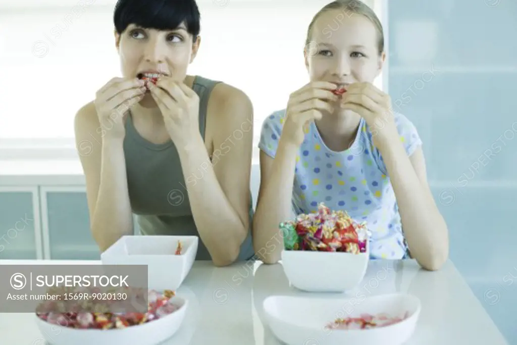 Woman and girl sitting side by side eating bowls of candy