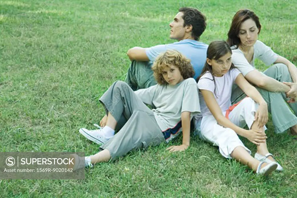 Family outdoors, sitting on grass back to back