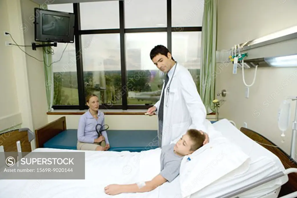 Child lying in hospital bed, doctor standing by side