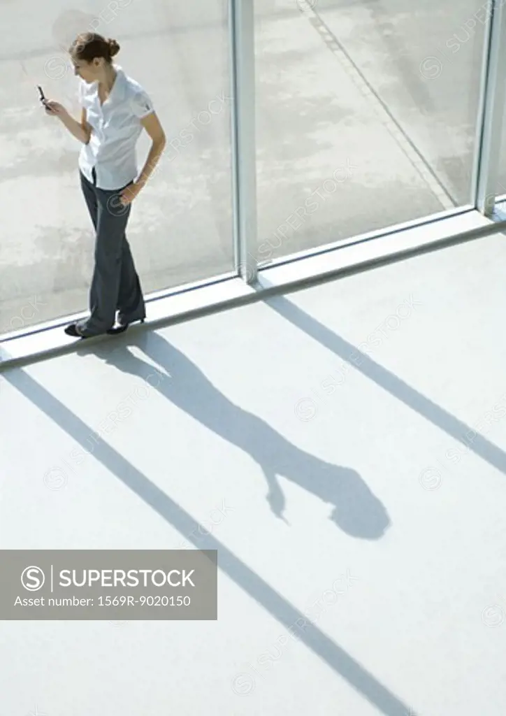Woman using cell phone by window, full length, high angle view