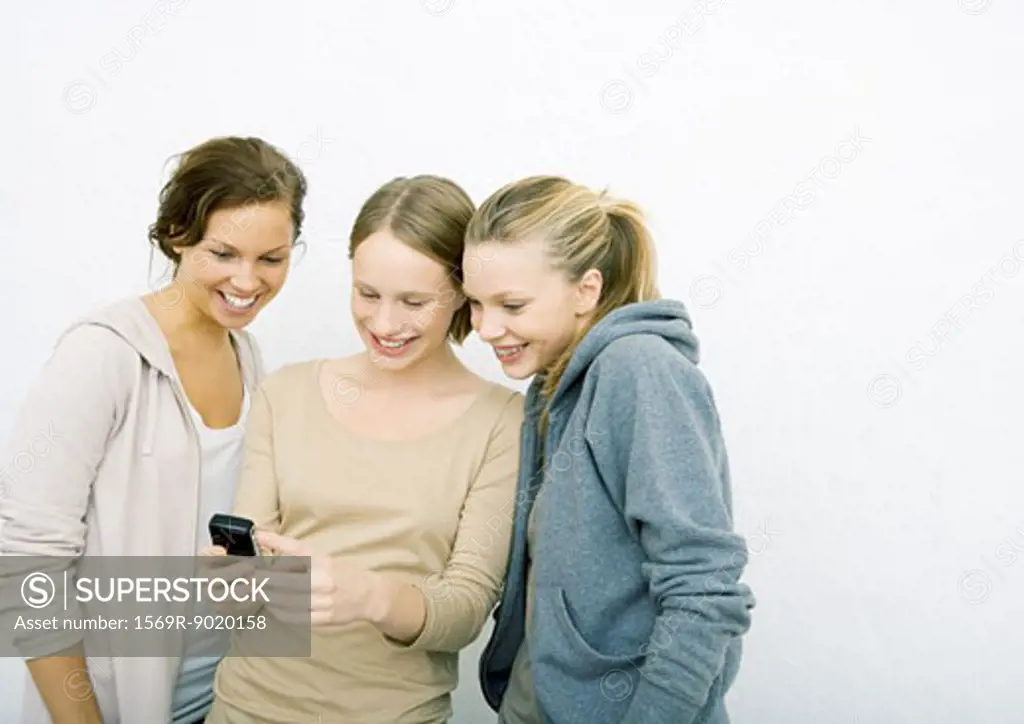 Three young female friends looking at cell phone together, smiling