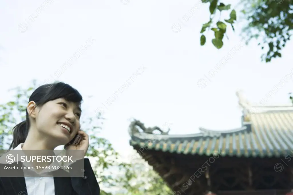 Woman using cell phone, traditional Chinese building in background
