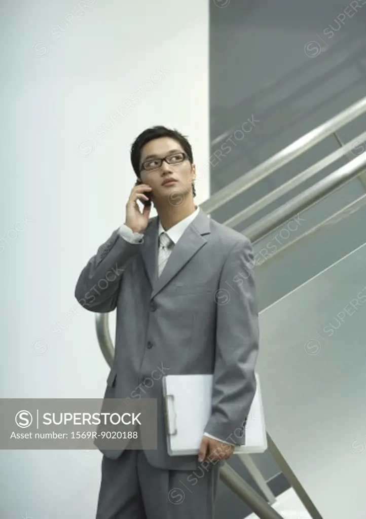 Businessman using cell, holding file, looking up