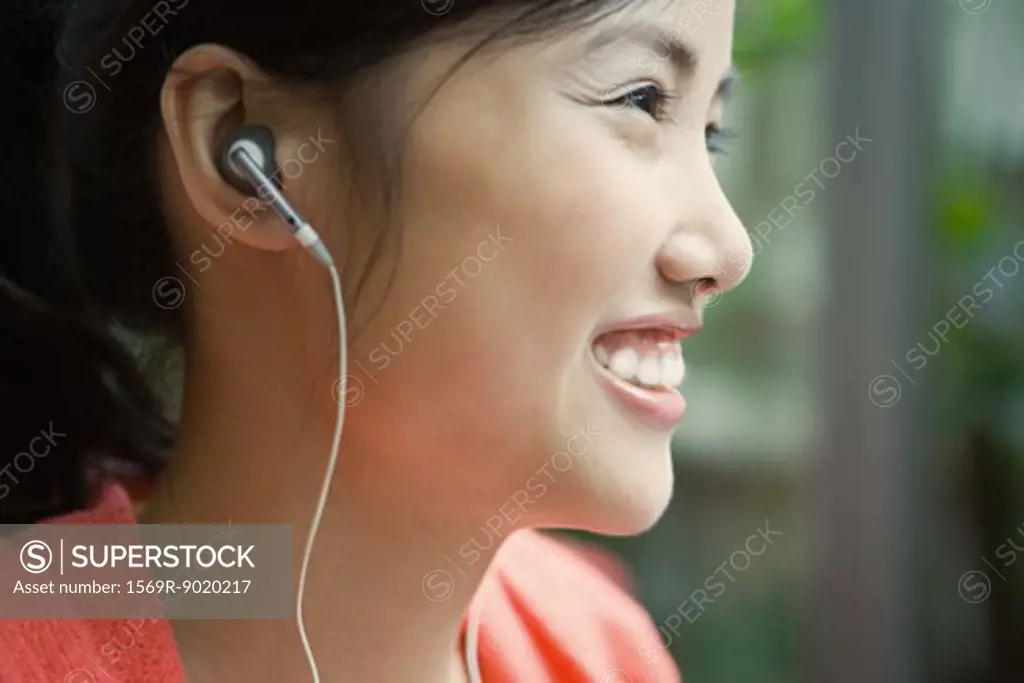 Young woman wearing earphones, smiling, close-up, profile