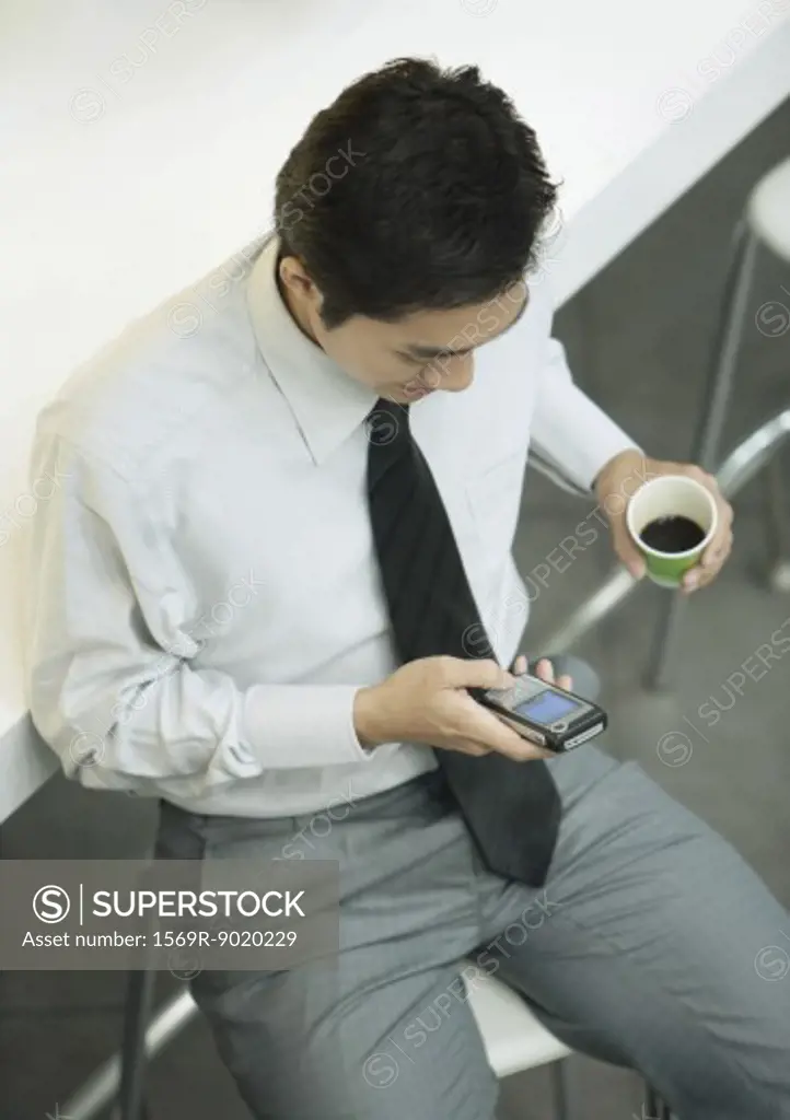 Executive holding cup of coffee and checking cell phone