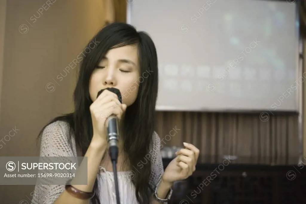Young woman singing karaoke, eyes closed