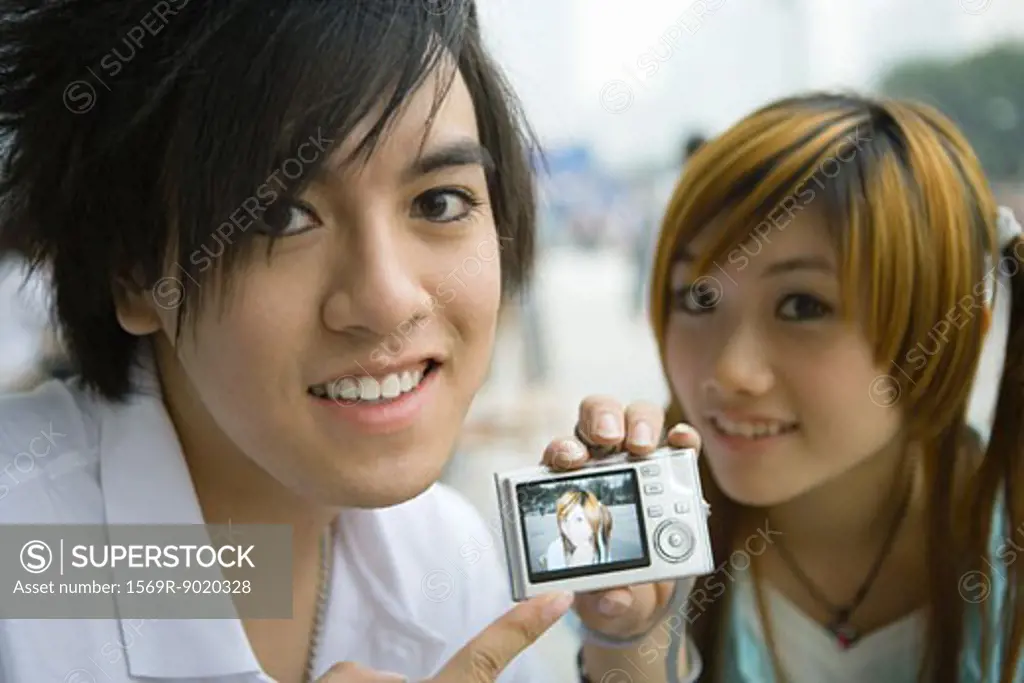 Teenage couple, man holding up digital camera showing photo of girlfriend 