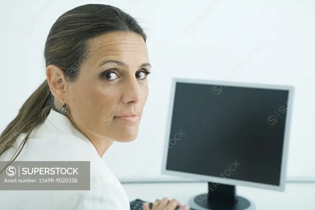 Businesswoman sitting at computer, looking over shoulder at camera
