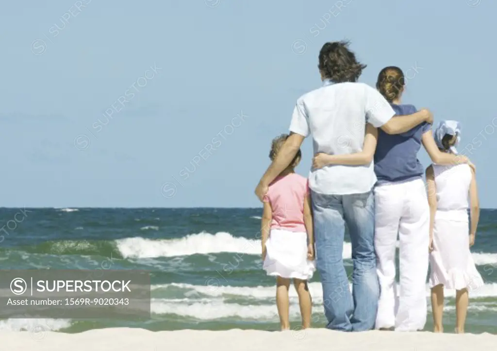 Family standing next to surf, facing ocean, rear view