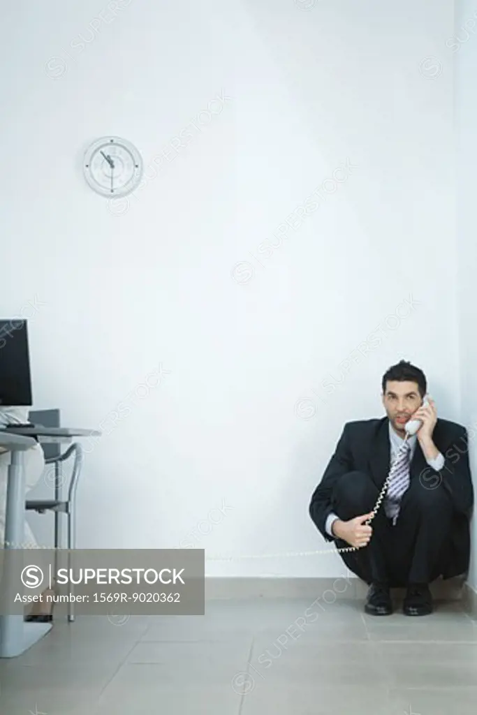 Businessman sitting on floor, in corner, talking on phone