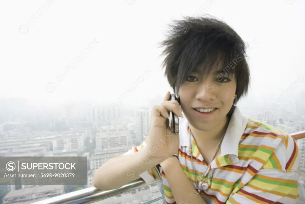 Teenage boy using cell phone, cityscape in background
