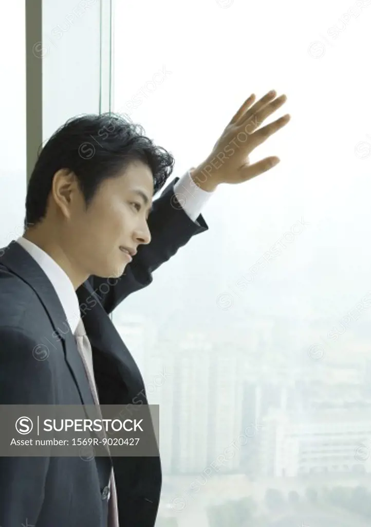 Businessman looking out of window of high rise, side view