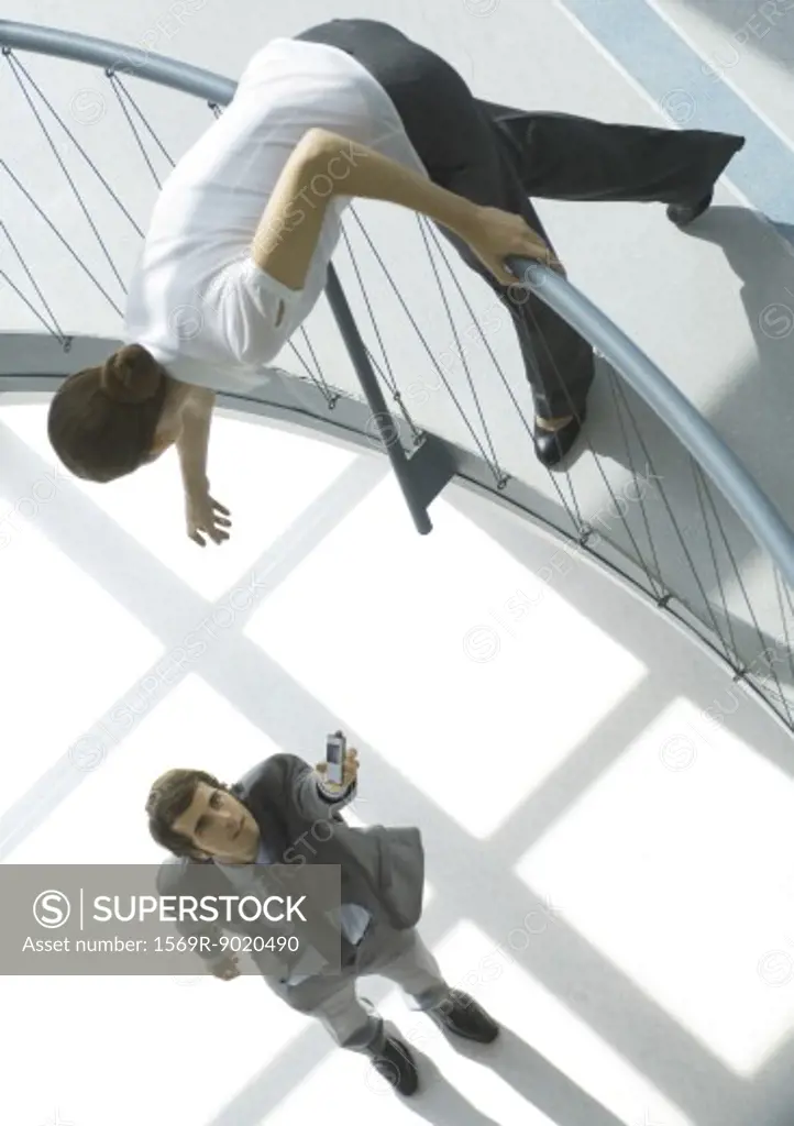 Businessman holding cell phone up to woman from lower floor, full length, high angle view