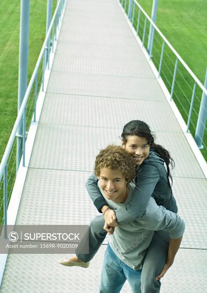 Teenage boy carrying teenage girl piggyback on walkway