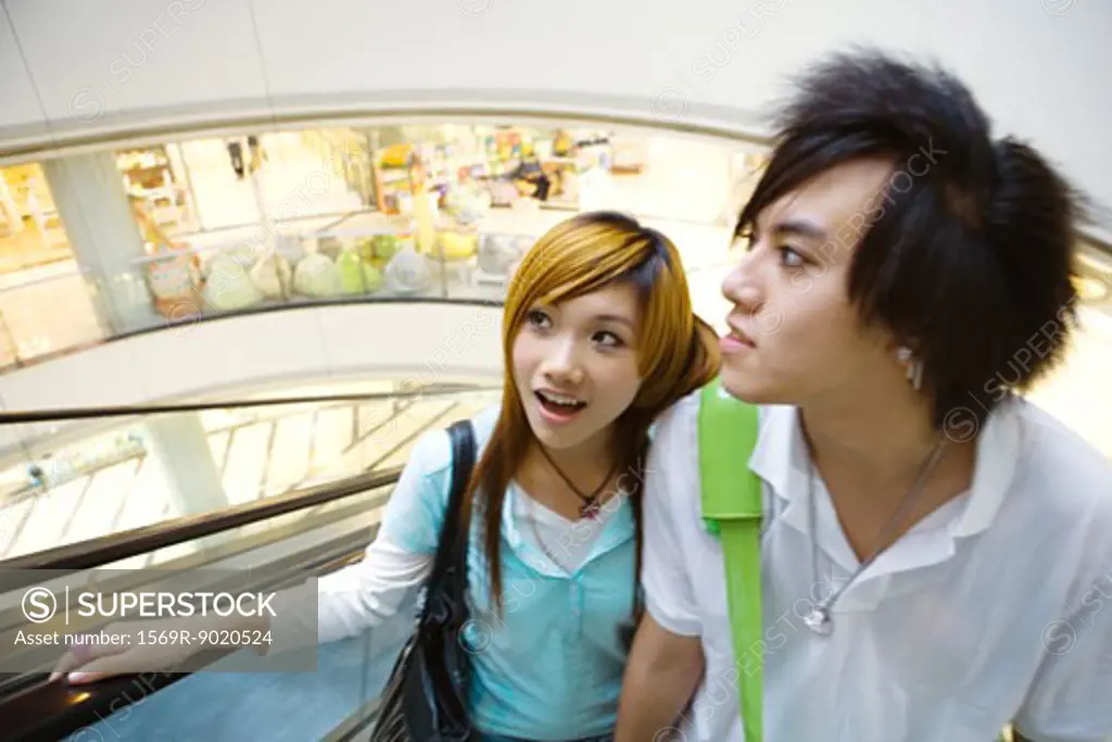 Teenage couple riding escalator in mall