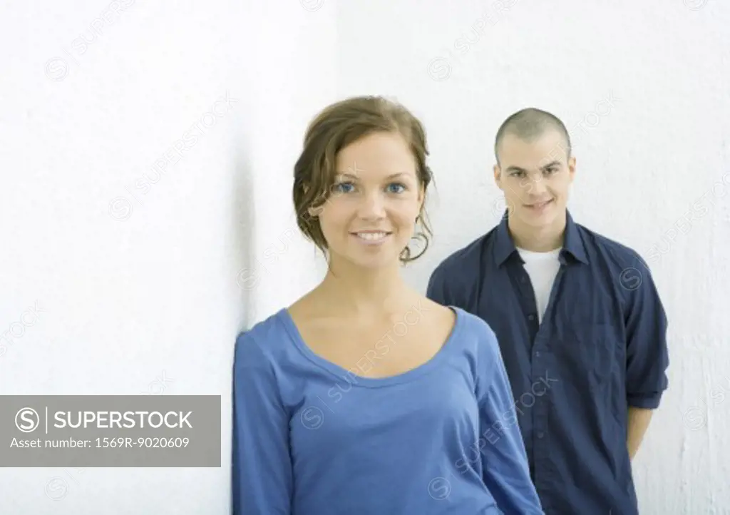 Young woman smiling at camera, young man behind her smirking