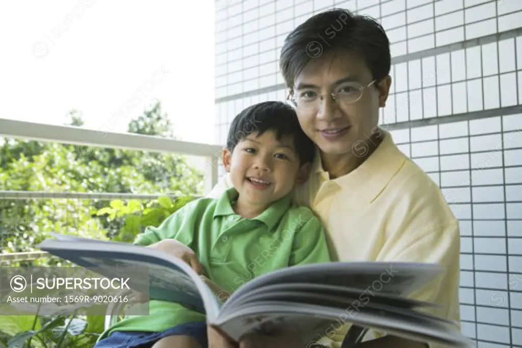 Father and son reading book, smiling at camera