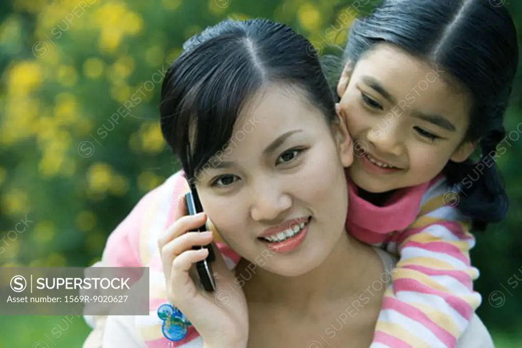 Woman using cell phone while girl leans over shoulder