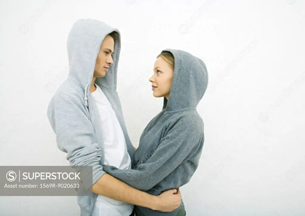 Young couple wearing hooded sweatshirts, holding each other around waist, face to face