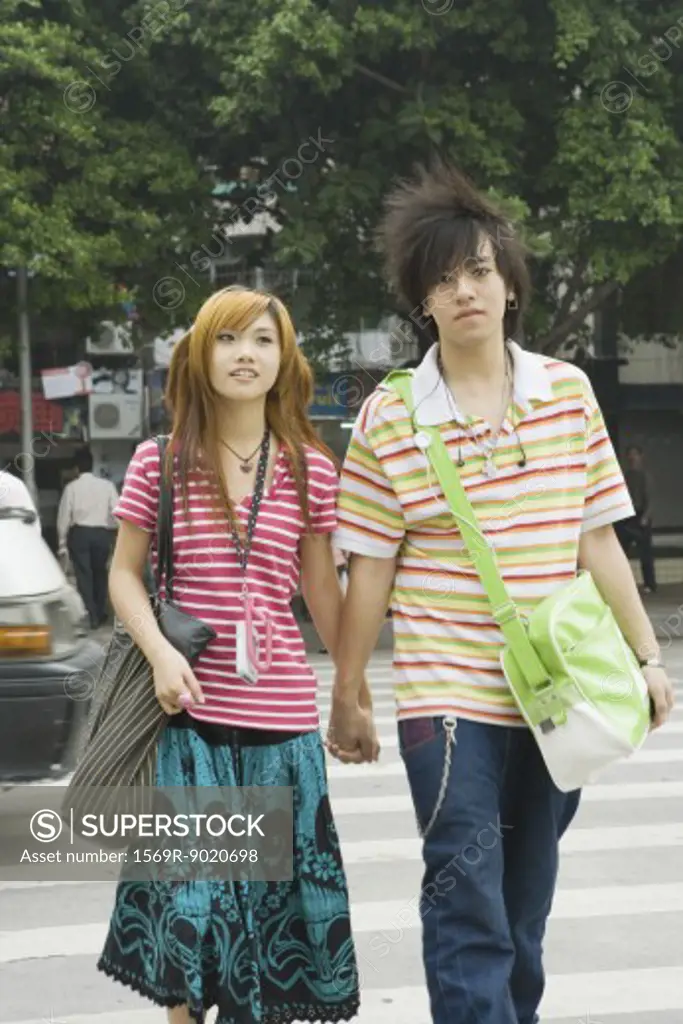 Young couple crossing street, holding hands, three quarter length