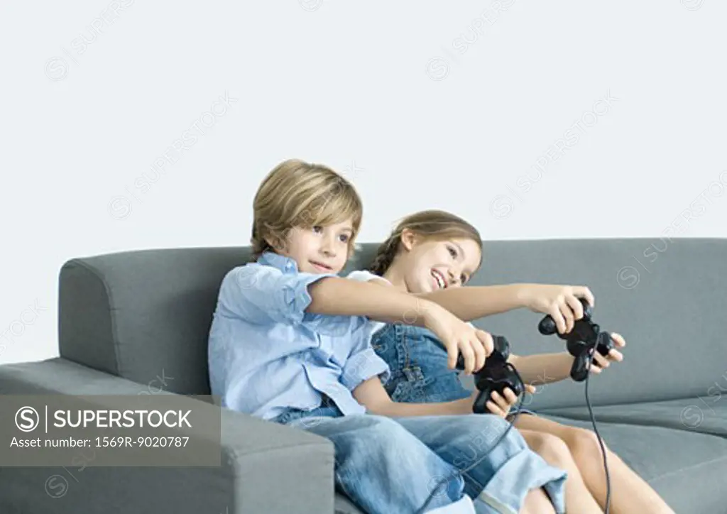 Boy and girl playing video game, holding out joysticks on sofa
