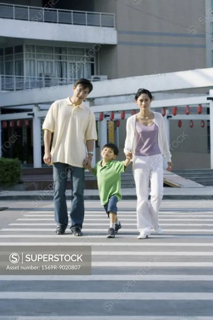 Boy crossing crosswalk, hand in hand with parents, full length