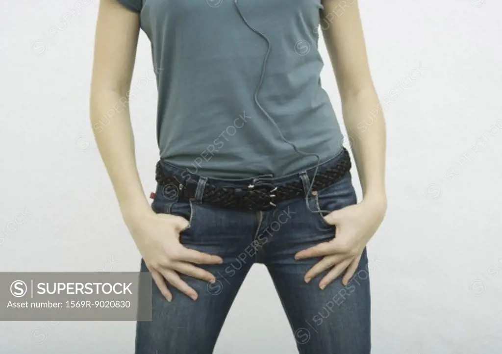 Young woman standing with thumbs in jean pockets, close-up of mid section