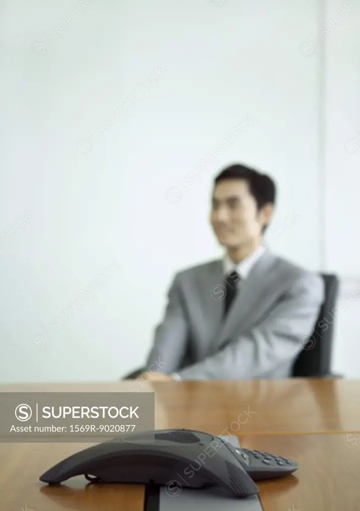 Businessman sitting at table, focus on conference phone in foreground