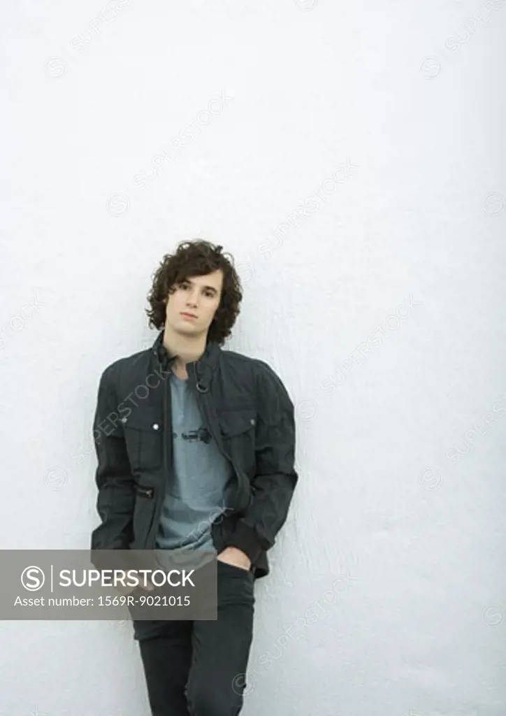 Young man leaning against wall with hands in pockets, portrait, white background