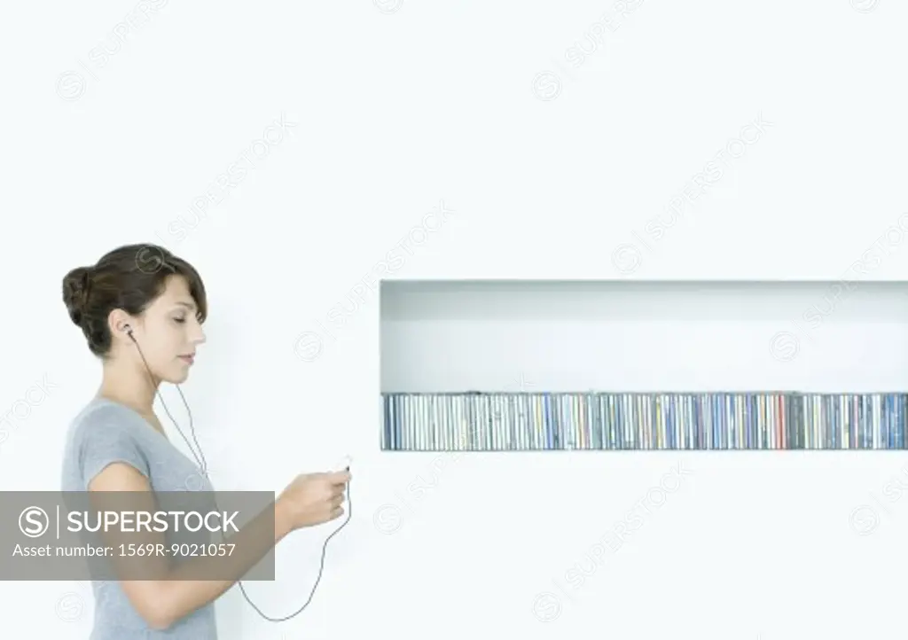 Young woman standing, listening to MP3 player, next to row of CDs, eyes closed
