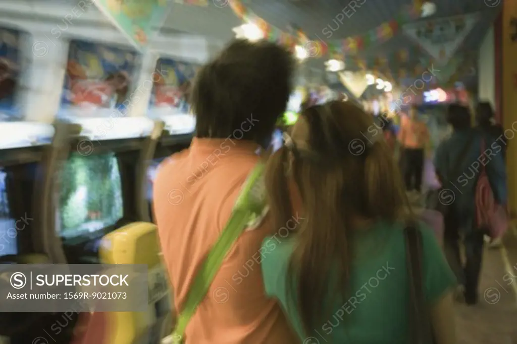 Young couple walking in video arcade, rear view
