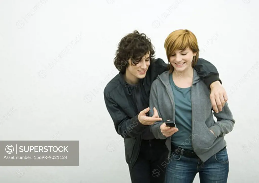Young adult couple, man with arm around woman, woman holding cell phone