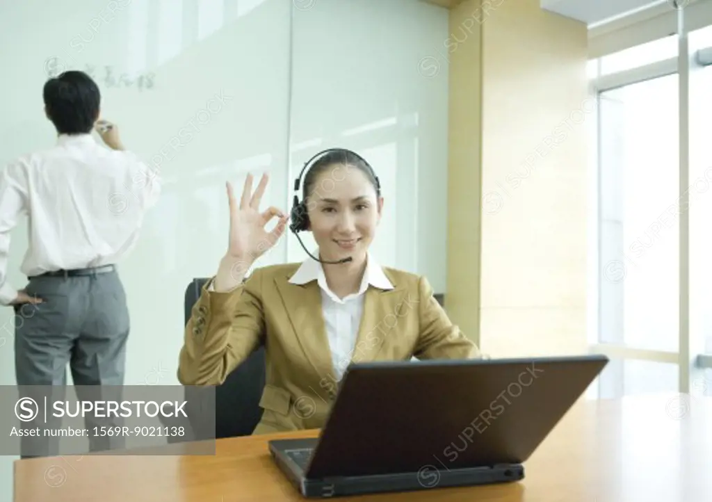 Businesswoman wearing headset and using laptop, making ok gesture