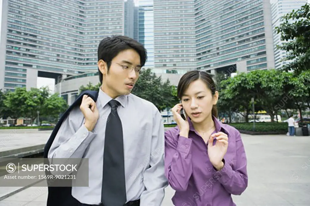 Two executives in business park, woman using cell phone