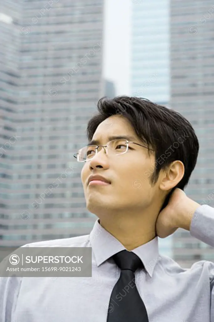 Businessman with hand on back of neck, looking up and frowning
