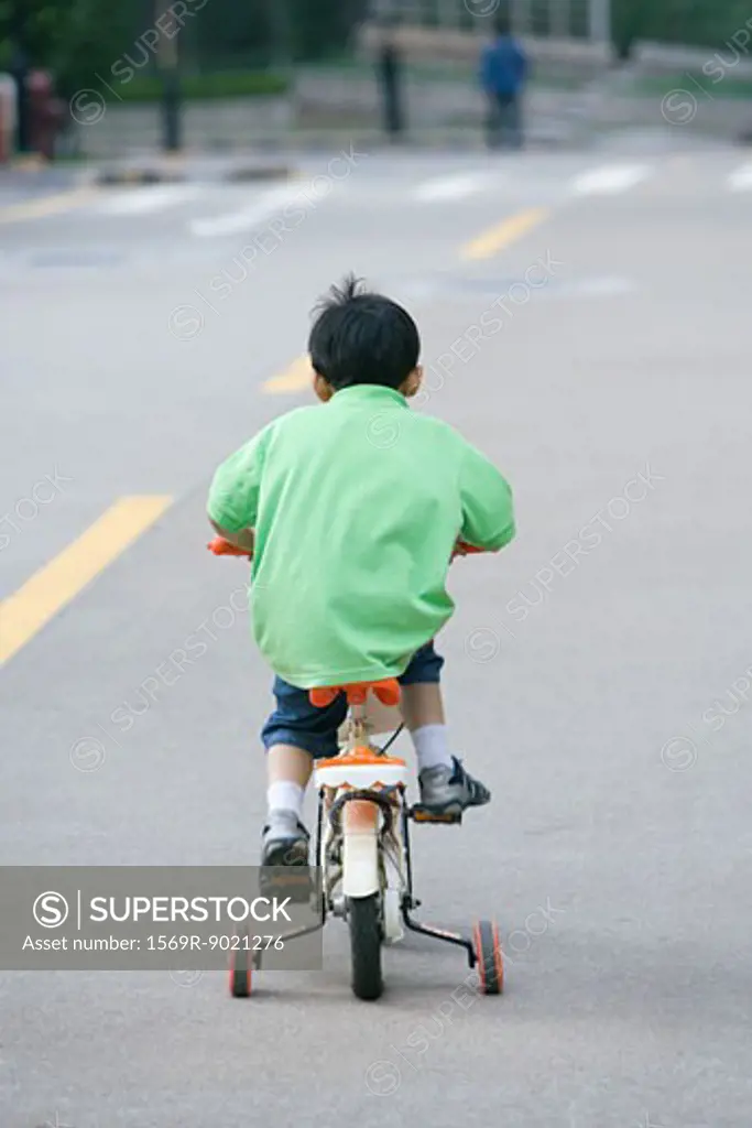 Boy riding bicycle with training wheels, rear view