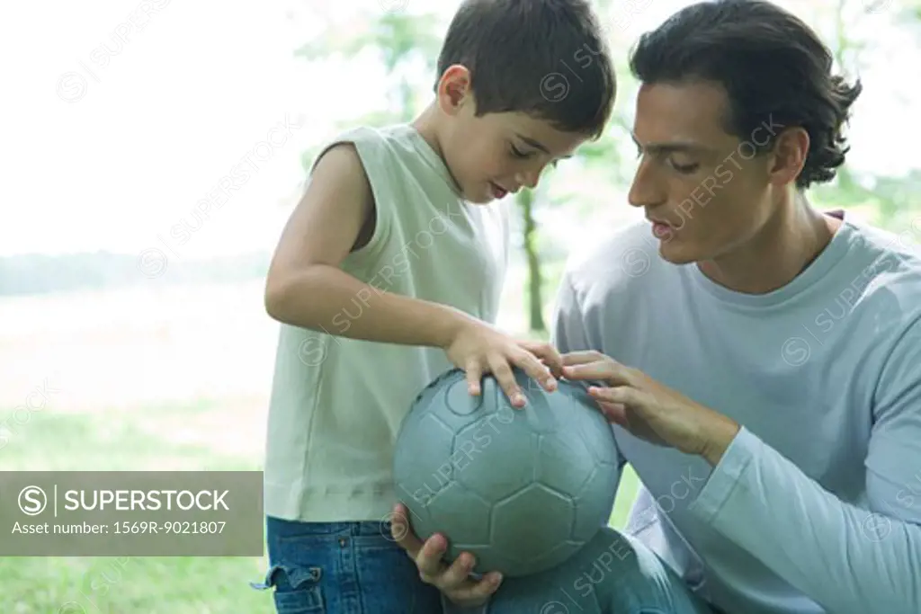 Boy looking at soccer ball with father