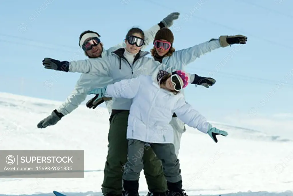 Young skiers standing on ski slope with arms out, full length portrait  