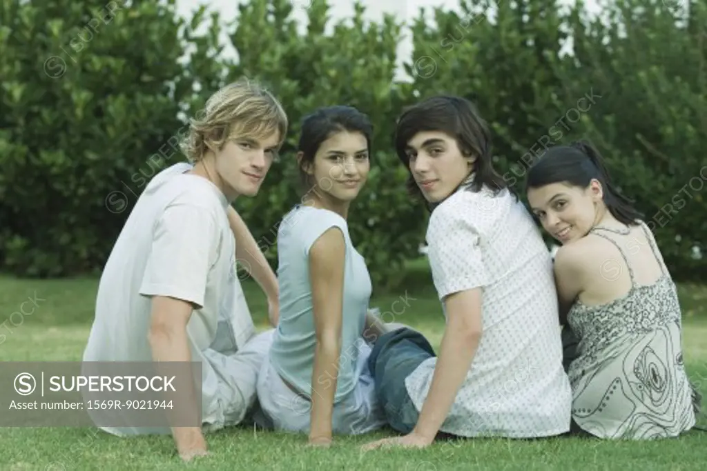 Group of young friends sitting on grass, looking over shoulders at camera