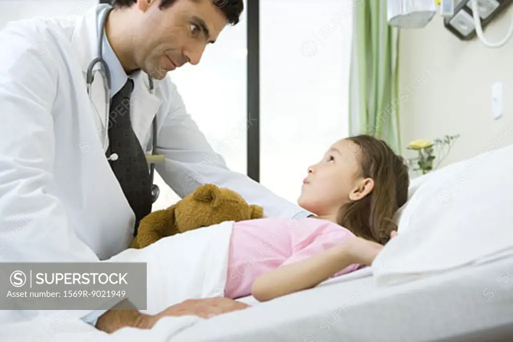 Doctor talking with girl lying in hospital bed